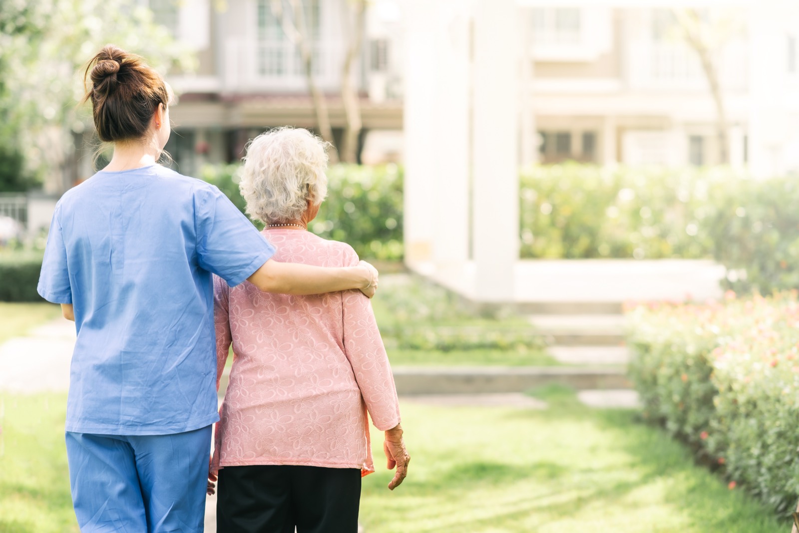 A nurse walking arm in arm with an older woman in a garden