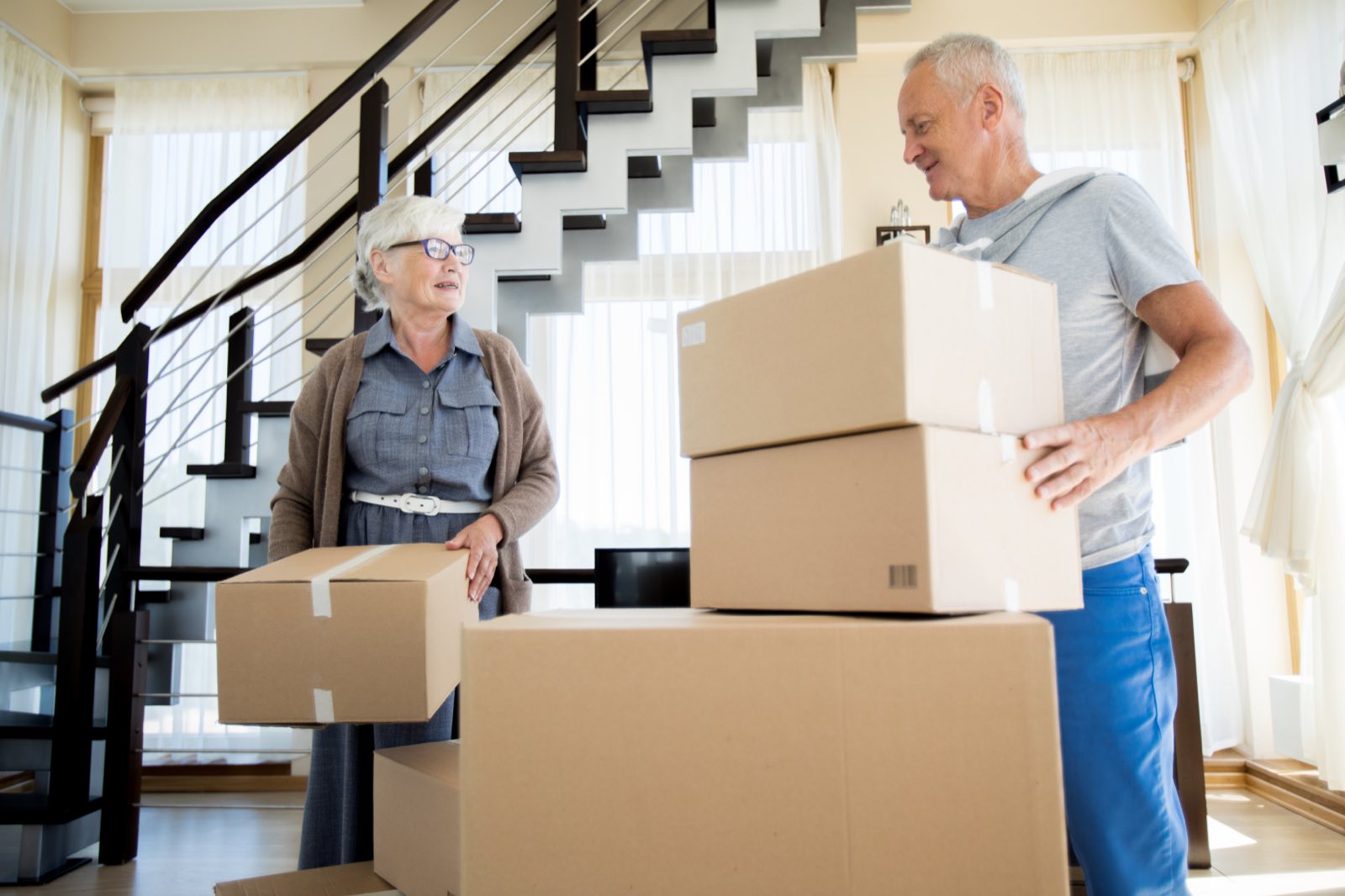 A retired couple carrying moving boxes in their home