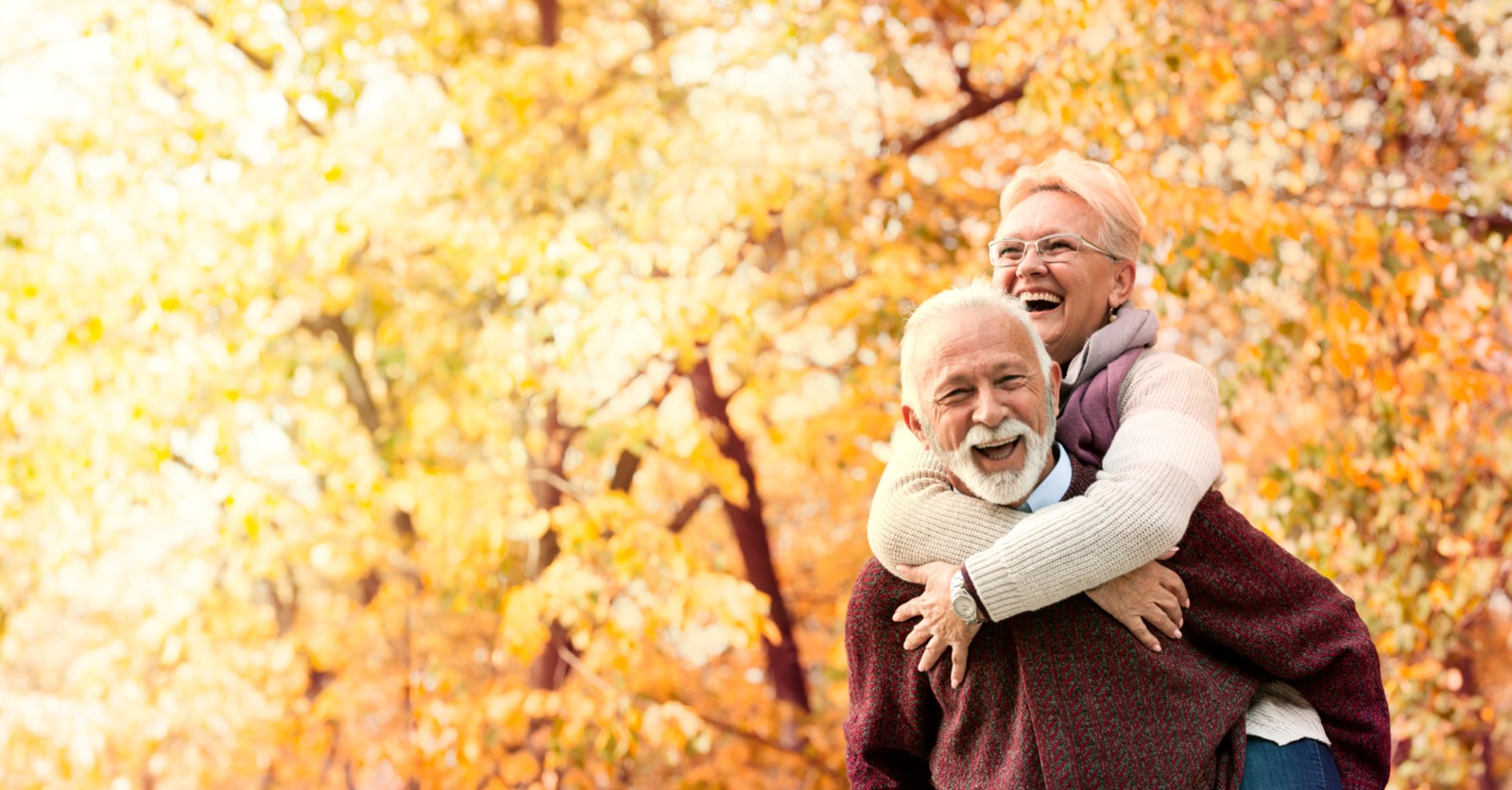 A laughing retired couple outdoors among autumn leaves